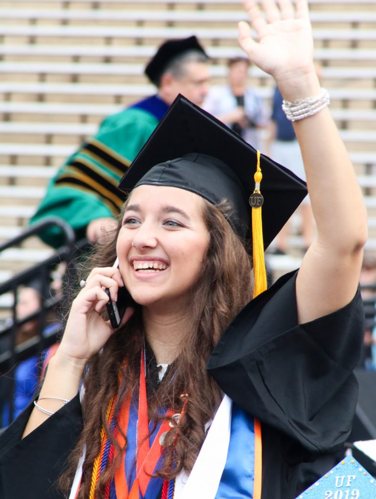 Graduating student waving at someone while on the phone