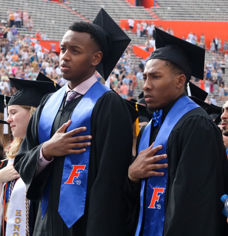 Two graduating students with their hands over their hearts
